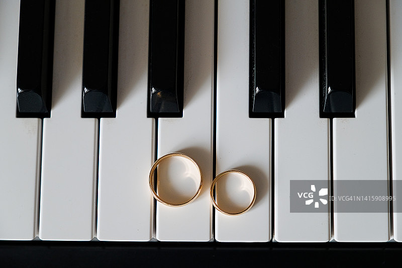金色的结婚戒指放在钢琴琴键上。浪漫，婚礼或订婚。爱的宣言。求婚。图片素材