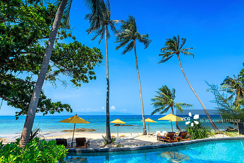 户外旅游景观。拥有游泳池、沙滩椅或躺椅的豪华海滩度假村，棕榈树和蓝天下的遮阳伞。暑期旅游和度假的背景概念图片素材