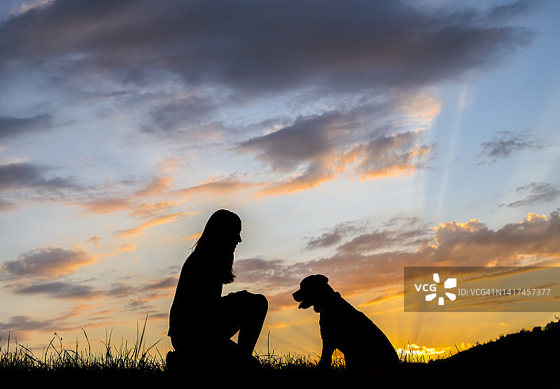 日落时，在云层中与狗玩耍的女人的剪影图片素材
