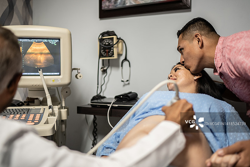 产科医生在他的医院办公室里用超声波扫描仪对怀孕的中成年妇女进行扫描图片素材
