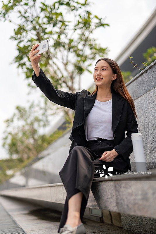 美丽年轻的亚洲女性办公室行政女士做视频通话与她的朋友在她的办公楼外图片素材