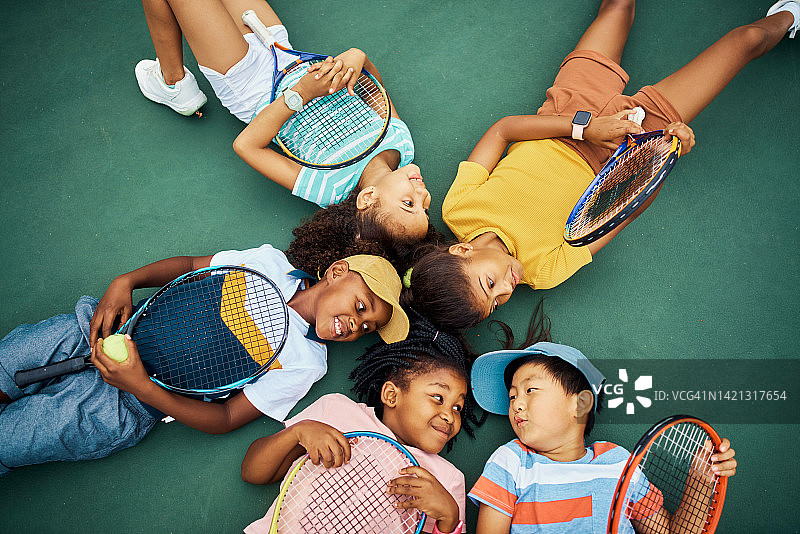 孩子们，网球和孩子们在网球场的地板上健身，锻炼和训练之前在体育俱乐部。快乐的女孩和男孩一起躺在地上，一起在户外玩有趣的游戏图片素材