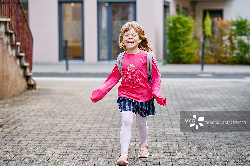 可爱的学龄前小女孩在上学的路上健康快乐的孩子步行到幼儿园和幼儿园。在户外的城市街道上，背着背包微笑的孩子。回到学校。图片素材
