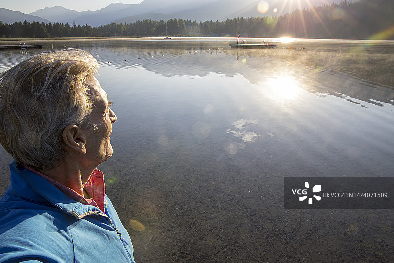 一位老人在日出时望着湖对面的山图片素材