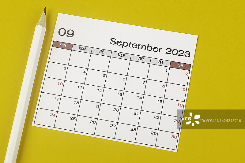 俯视图日历桌2023:家庭办公室手工使用。九月是组织者用白色铅笔在黄色纸背景下计划和截止日期的月份。图片素材
