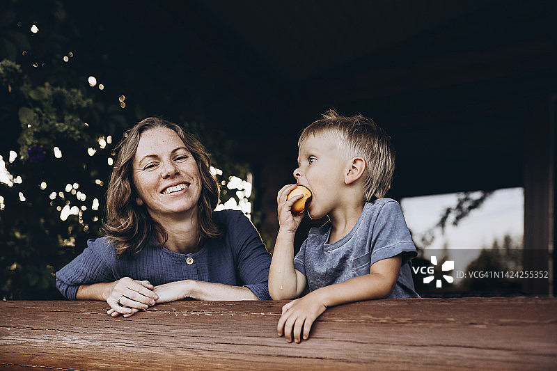 男孩和微笑的母亲在阳台上吃水果图片素材