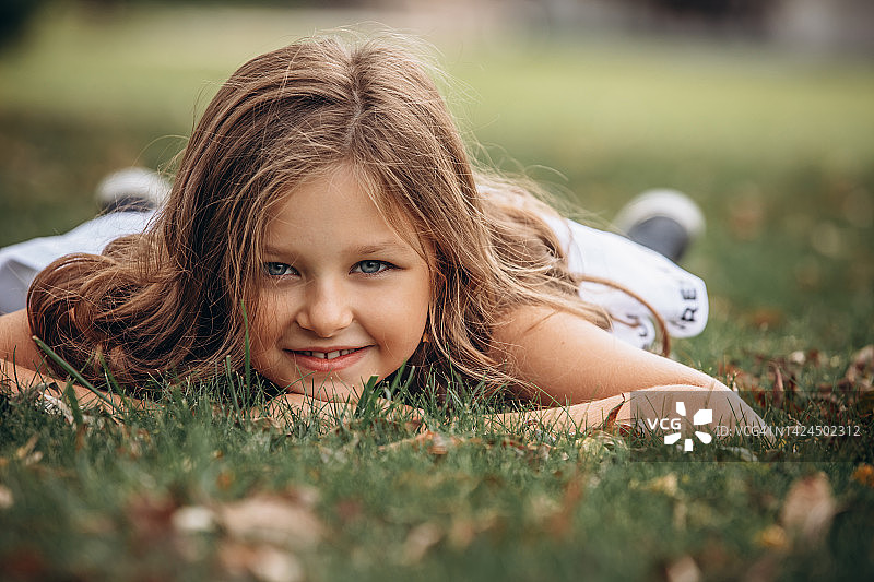 美丽的小女孩穿着白色的裙子，画像躺在草地上图片素材