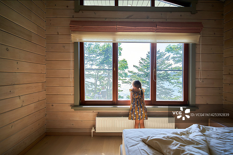 女孩站在靠窗的房间里，窗外是美丽的自然风景。图片素材