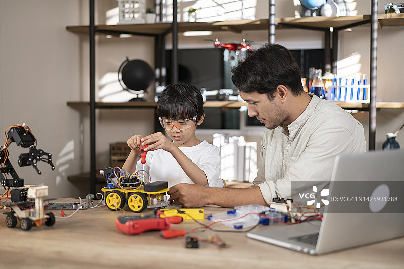 一个亚洲男孩和他的父亲在家里做了一个玩具机器人。图片素材