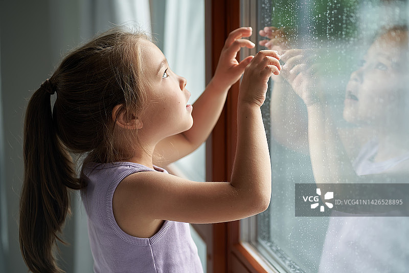 一个女孩站在窗边看雨。图片素材