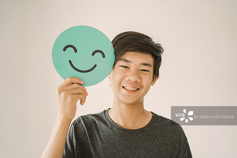 快乐混合的亚洲少年抱着微笑的表情符号脸，积极的心理健康理念图片素材