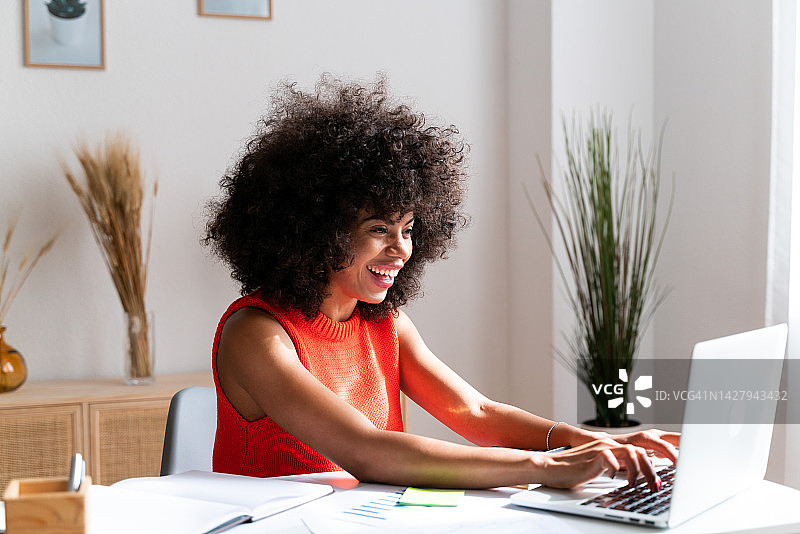 微笑的非裔美国妇女在家工作，在她的笔记本电脑上打字图片素材