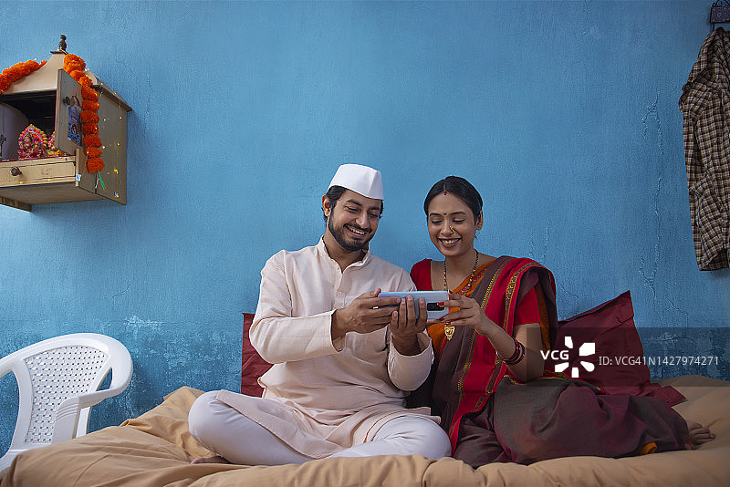 马哈拉施特拉的一对夫妇坐在家里的小床上一起使用智能手机图片素材