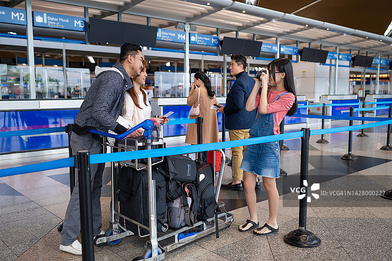 亚裔华人家庭在机场柜台排队办理行李托运手续时正在拍照。图片素材