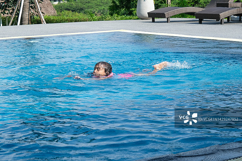暑假期间，小女孩在热带度假胜地的室外游泳池玩耍。孩子们正在学习游泳。孩子们的健康夏季活动。图片素材