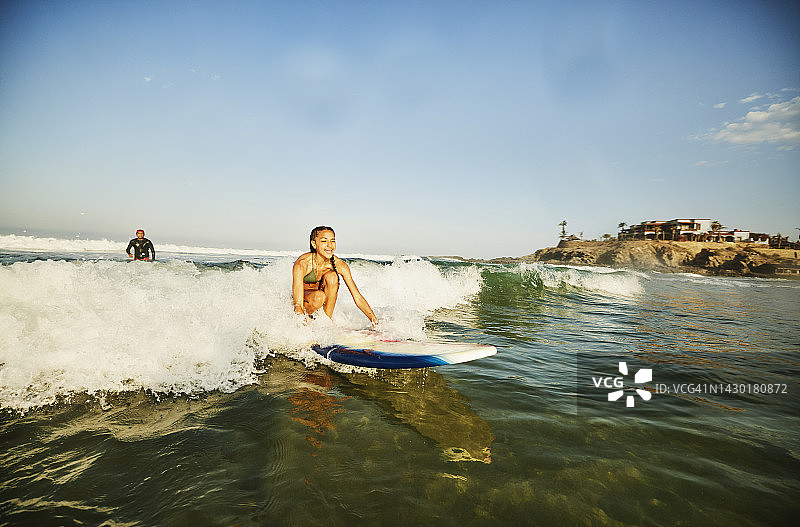 广角拍摄的微笑的女孩骑波，同时上冲浪课图片素材