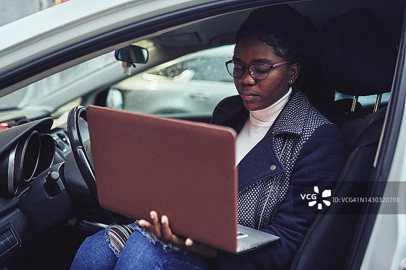 一位年轻女子坐在车里，拿着笔记本电脑，在网上工作或学习。图片素材