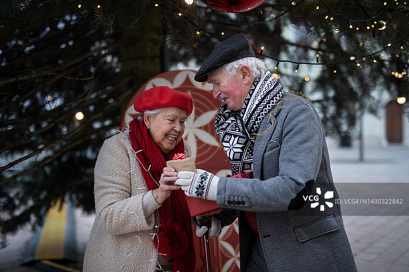 老年人夫妇在市中心户外的圣诞树下互赠礼物。图片素材