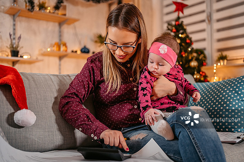 母亲一边在家里抱着孩子过圣诞节，一边计算着财务账单图片素材