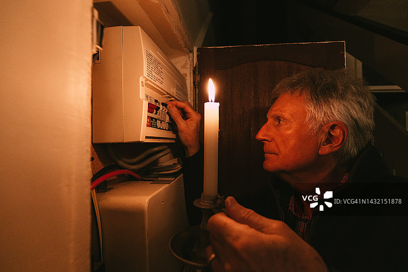 停电期间，老人在烛光下检查家用保险丝盒图片素材