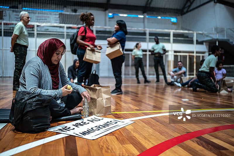 一名难民妇女坐在避难所的地上，旁边写着“我们都是移民!”图片素材