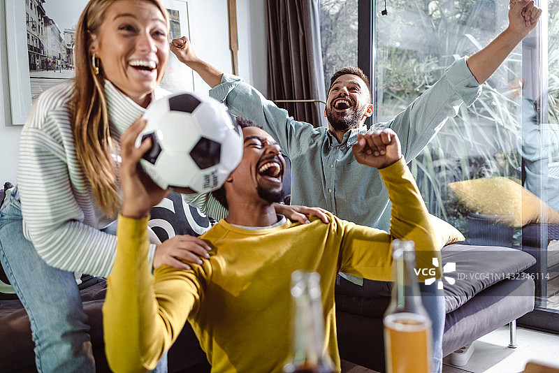 一群兴高采烈的朋友在看电视上的足球比赛，庆祝进球图片素材