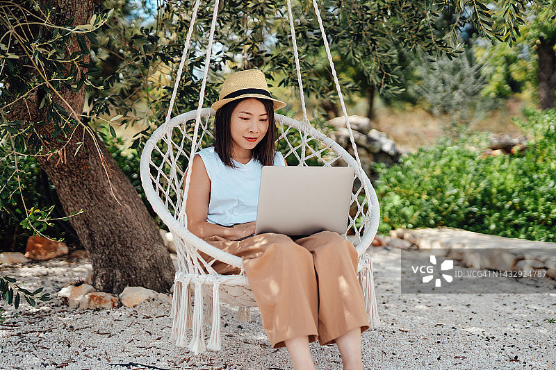 年轻女子在花园秋千椅上用笔记本电脑工作图片素材