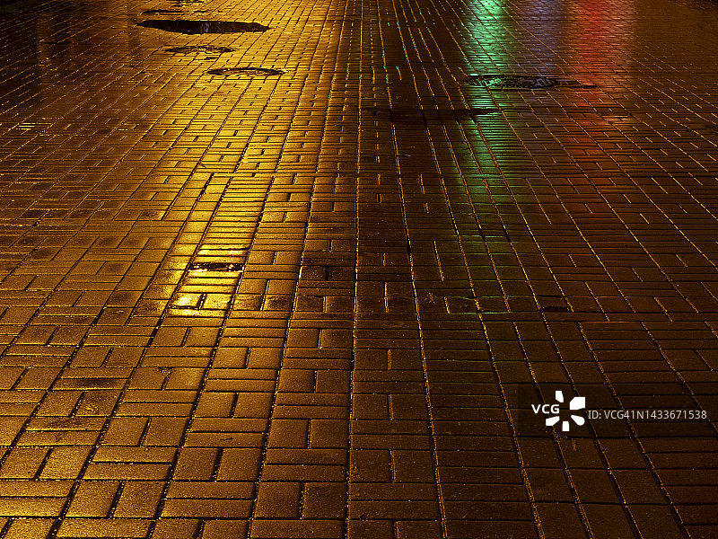 城市灯光在潮湿的鹅卵石上的黄、绿、红的倒影图片素材