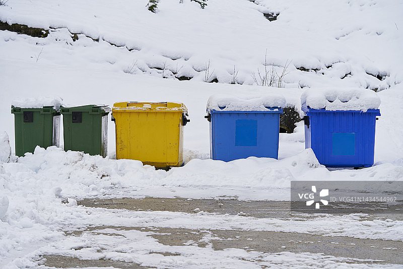 在寒冷的冬天，五颜六色的回收垃圾桶被积雪覆盖。图片素材