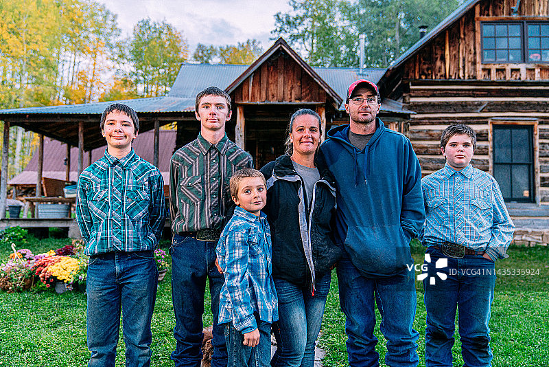 在美国科罗拉多州，一个白人牧场家庭在他们的小镇家庭农场辛苦工作了一天后，站在他们小屋风格的房子前面图片素材