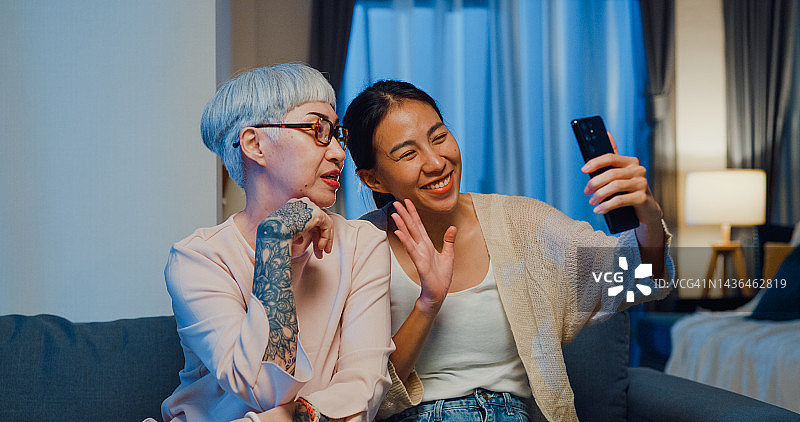 快乐的亚洲家庭，年幼的女儿和年长的妈妈教年长的妈妈使用智能手机与朋友在线视频通话，周末晚上在家打发时间。图片素材
