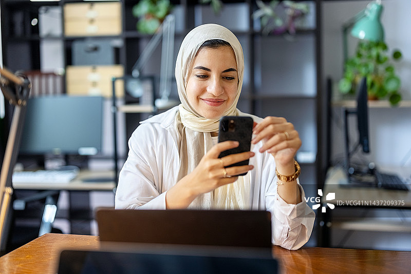 快乐的年轻穆斯林妇女在办公室使用手机图片素材