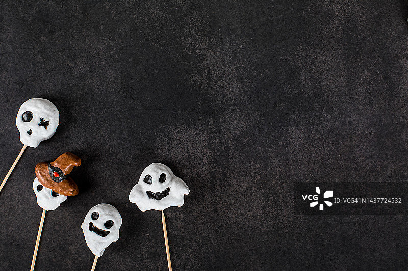 节日万圣节。主题饼干的形状是幽灵和戴着帽子的骷髅头，上面覆盖着糖霜，放在一根木棍上。黑暗的灰色背景。前视图。本空间图片素材
