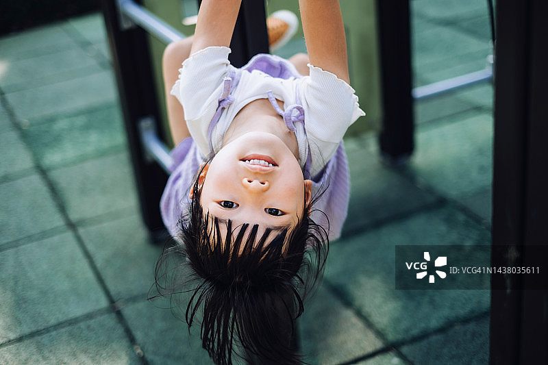 快乐的亚洲小女孩在操场上玩得很开心，倒挂在攀爬架上。看着镜头。童年的生活方式。户外趣味、无忧无虑、自由的理念图片素材