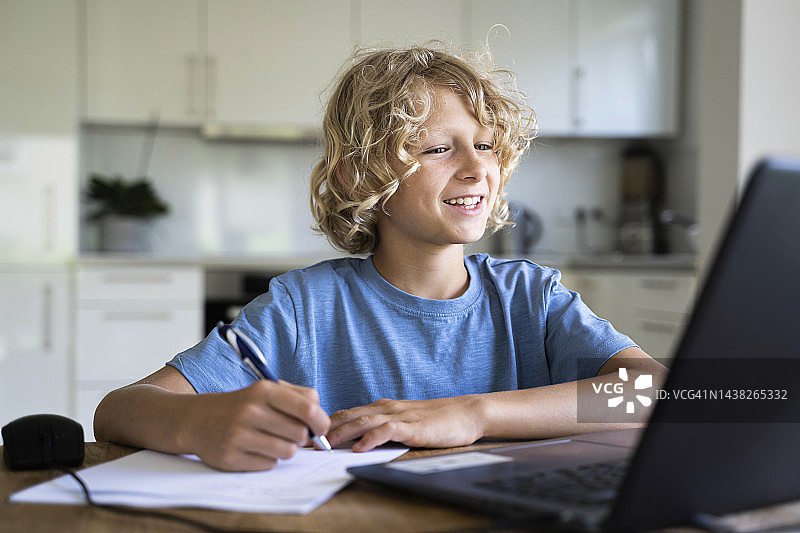 快乐的男孩在家里看笔记本电脑做作业图片素材