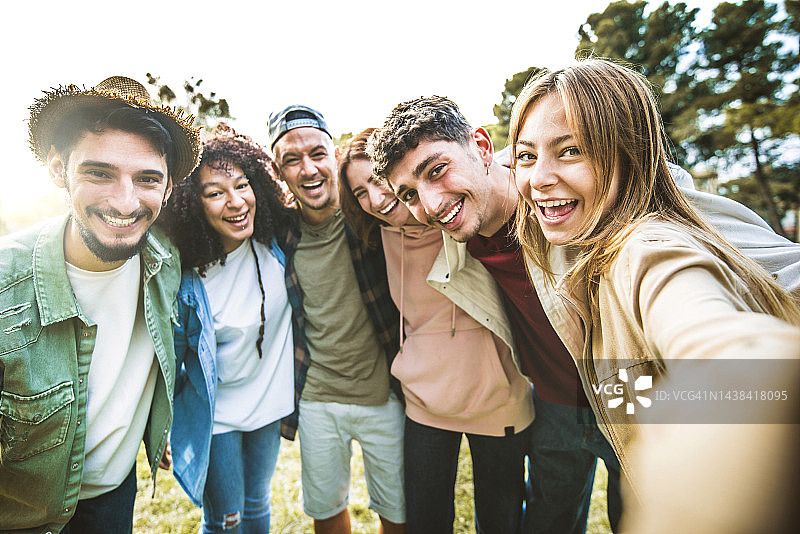 快乐的年轻人在户外一起对着镜头微笑-公园里一群快乐的朋友用智能手机自拍肖像-青春和友谊的概念图片素材