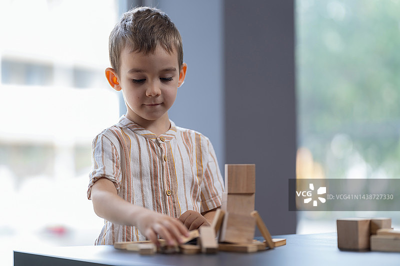 一个男孩在家里玩木制玩具块图片素材