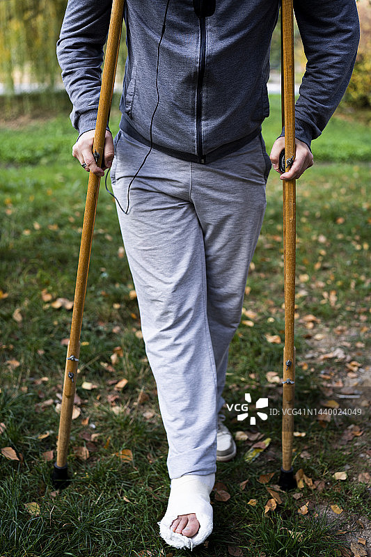 一个断腿的年轻人，拄着拐杖走路。图片素材