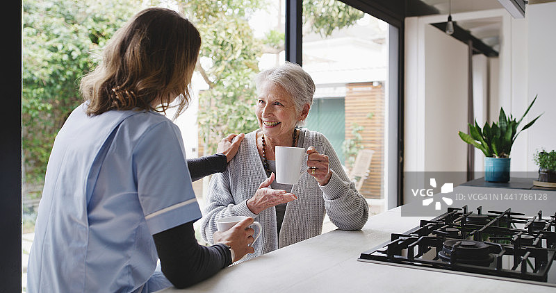 保健方面，高级护士和老妇人带着早晨的咖啡在厨房微笑着。医护人员、妇女和幸福的人们在养老院幸福地交谈图片素材