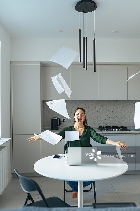 工作压力大，工作过度。压力大的中年妇女在家庭办公室工作时向空中扔文件图片素材