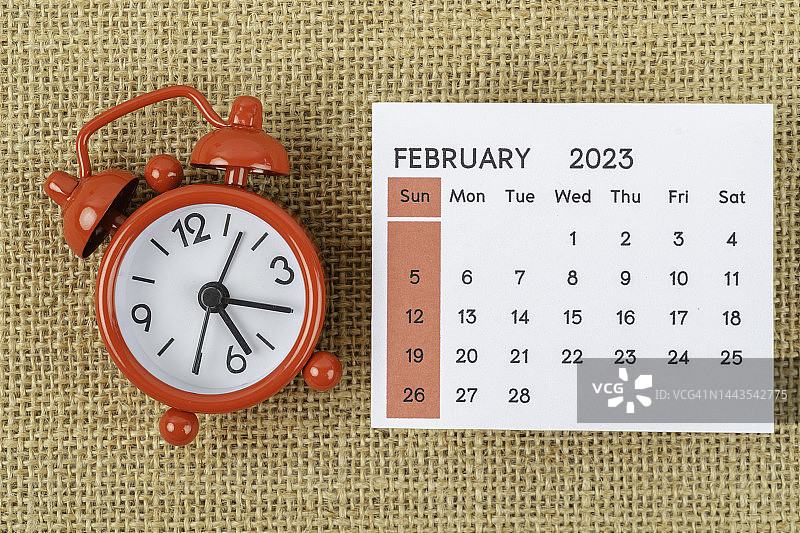 2023日历台:2月是组织者计划和截止日期的月份，在粗麻布背景上有一个闹钟。图片素材