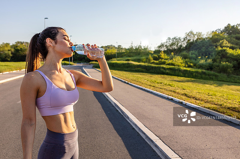 年轻女子从瓶子里喝水的照片。白种女性在运动或运动后喝水。图片素材