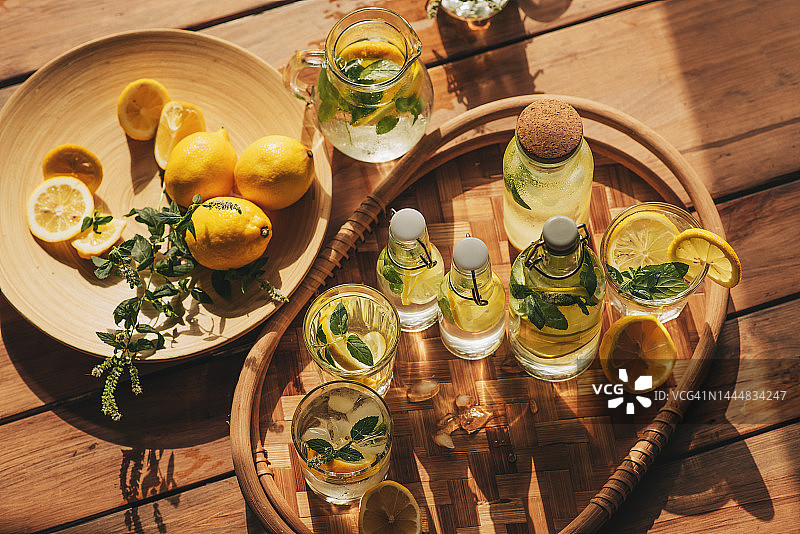 柠檬水装在玻璃杯和瓶子里，放在户外的木桌上。夏日清爽饮品。加柠檬的凉水排毒图片素材