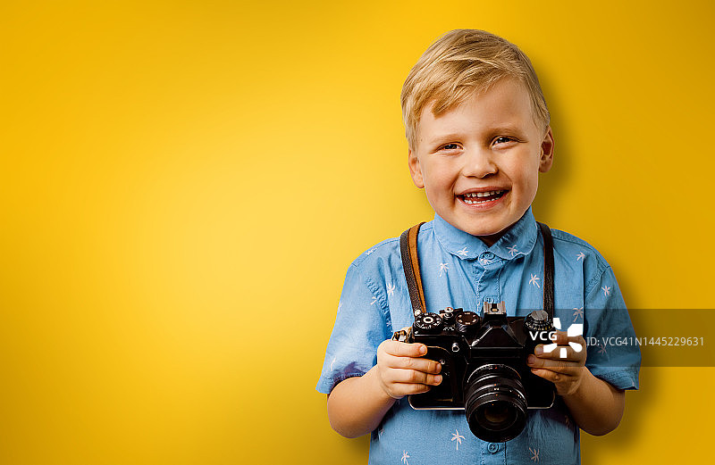 小微笑的男孩与复古相机在一个黄色的背景与复制空间。儿童摄影师图片素材
