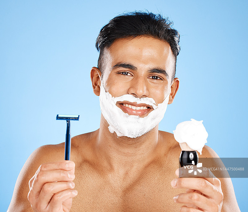 男子，剃须刀和剃须膏护肤，美容或面部治疗对蓝色工作室背景。肖像的男性胡须与微笑持有化妆品剃须，美容或卫生的模型图片素材