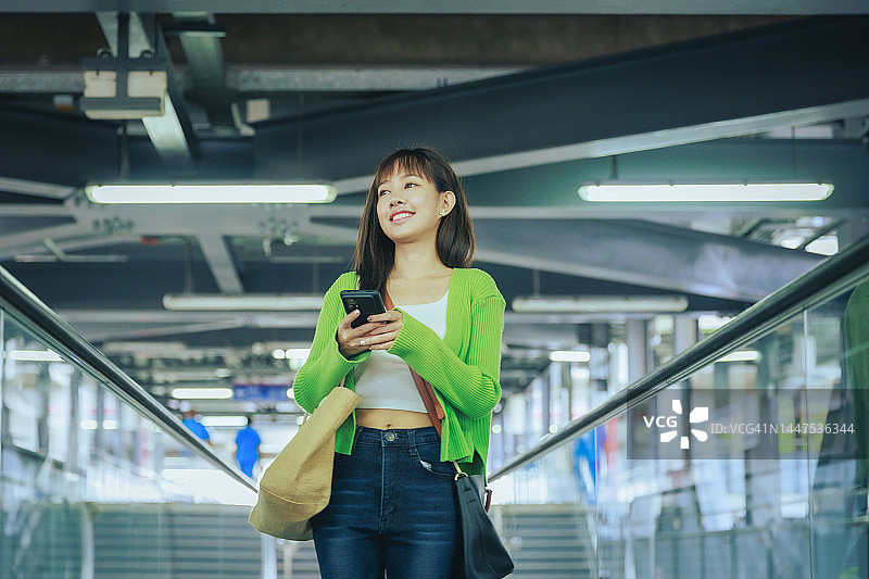 年轻的亚洲女商人在机场乘坐自动扶梯时用手机阅读电子邮件。商务旅行的概念。图片素材