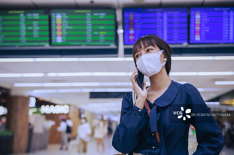 年轻的亚洲女商人戴着口罩在机场离境区打电话。商务旅行的概念。图片素材