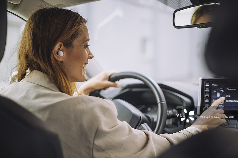 微笑的女商人戴着无线入耳式耳机，使用汽车仪表板控制面板图片素材