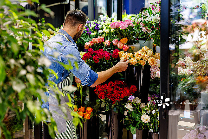 一位男花匠正在花店的冰箱里摆放鲜花。图片素材