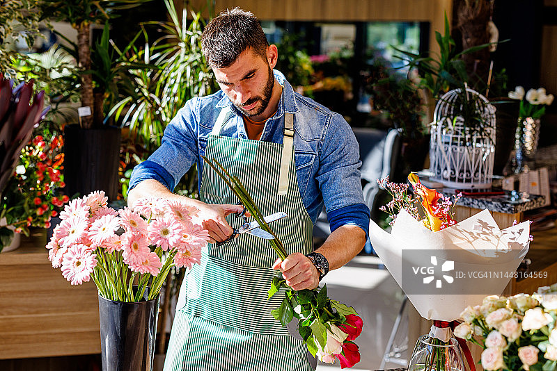 在一家现代花店里，一位年轻的花匠正在用剪刀准备一束玫瑰花。图片素材